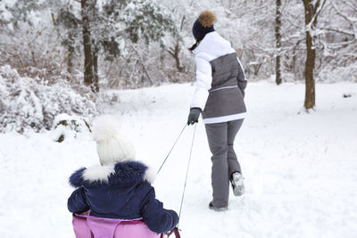 Mom takes his little daughter on a sledge uphill through the winter snow 