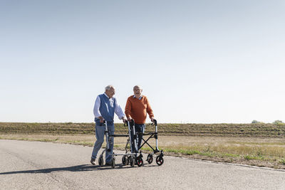 Two old friends walking on a country road, using wheeled walkers