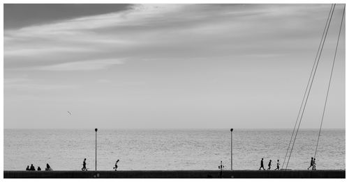 Silhouette people on retaining wall by sea against sky