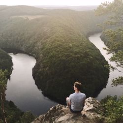 Rear view of man sitting on rock by river