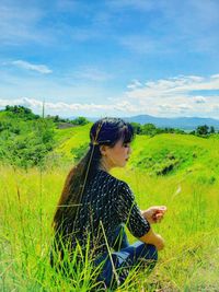 Rear view of young woman sitting on field against sky