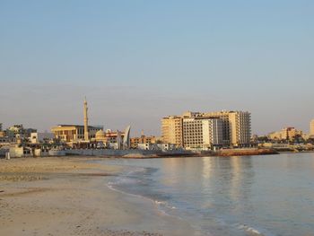 City buildings by sea against clear sky