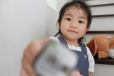 Portrait of cute baby girl playing phone cover while sitting on steps at home