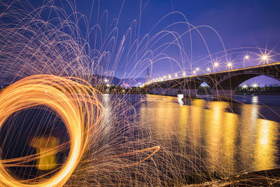 Man spinning wire wool by river at night