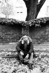 Portrait of young woman sitting on brick wall