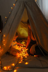 Mother with daughter sitting in illuminated tent