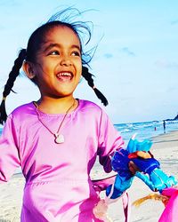 Portrait of happy girl standing at beach against sky