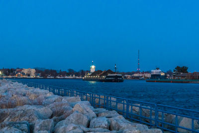 Illuminated buildings by sea against blue sky