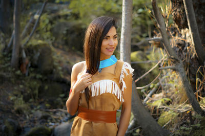 Smiling young woman in traditional clothing standing against trees