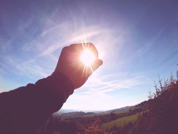 Person hand holding sun against sky during sunset