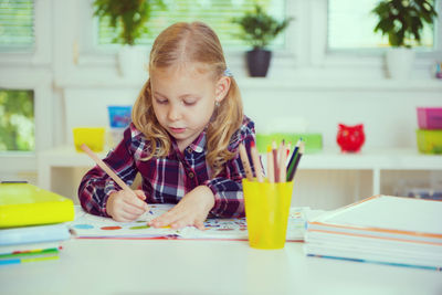 Girl drawing on book while sitting on table at home