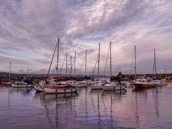 Sailboats moored in harbor at sunset