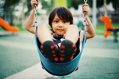 Portrait of boy sitting on swing at playground