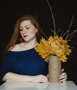 Beautiful woman holding dry maple leaves in vase