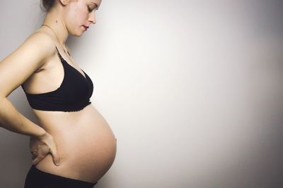 Side view of pregnant woman standing by wall
