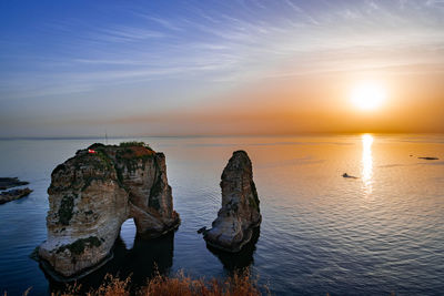 Rock formation in sea against sky during sunset