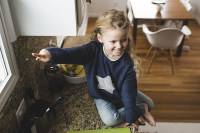 High angle view of girl pointing while sitting on kitchen counter at home