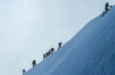 Low angle view of people on snow covered mountain against sky