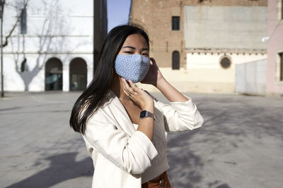 Young woman with protective face mask on footpath during sunny day