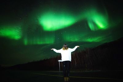 Woman with arms outstretched standing against aurora borealis at night