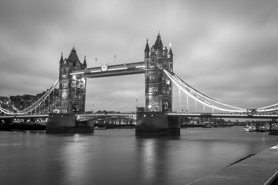 Illuminated tower bridge over thames river against sky