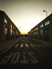 Road by buildings against sky during sunset