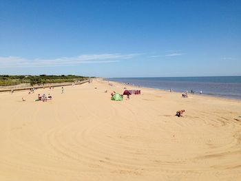 People on beach against clear blue sky