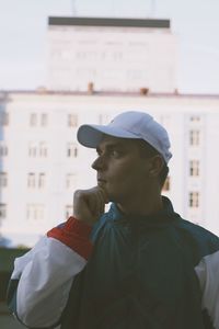 Man with hand on chin looking away while standing against building