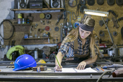 Woman writing in book while standing against work tools