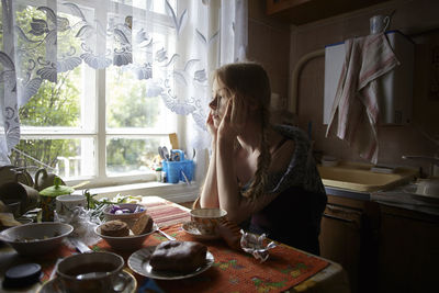 Thoughtful woman with hands on chin looking away while sitting by table at home