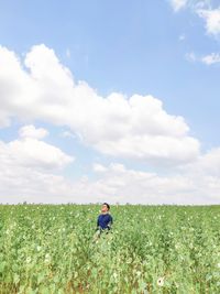 Young man standing amidst flowering plants on field against sky