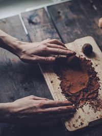 Cropped hands of person by cocoa powder on cutting board