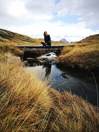 Man sitting by lake against sky