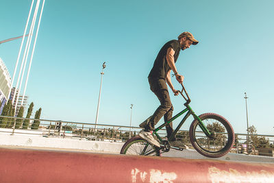 Side view of young man riding bicycle against clear sky