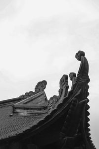 Low angle view of statue on roof against sky