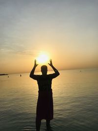 Man standing in sea against sky during sunset