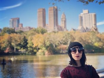 Portrait of woman wearing sunglasses against lake in city