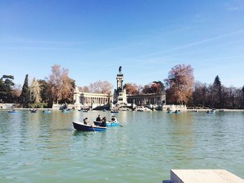 Man and woman in boat on lake against blue sky at buen retiro park