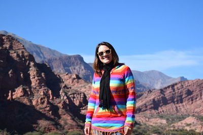 Portrait of smiling young woman standing on mountain against clear sky