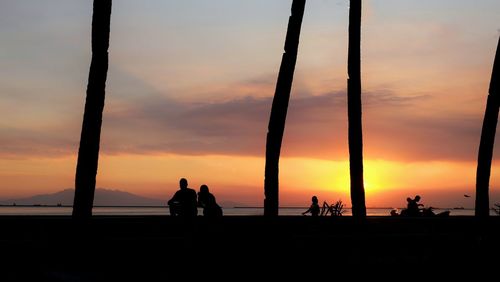 Silhouette people at beach against sky during sunset