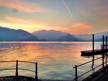 Scenic view of lake and mountains against cloudy orange sky during sunset