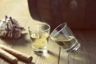 Close-up of rum in shot glasses and cigars by barrel on table