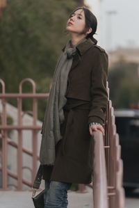 Portrait of young woman standing against railing