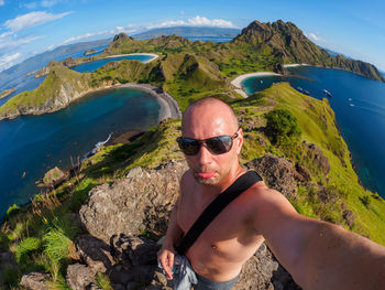 Fish-eye lens portrait of shirtless man standing on cliff by sea