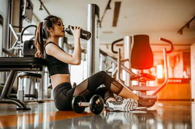 Tired woman drinking water while exercising in gym