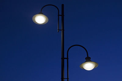 Low angle view of illuminated street light against blue sky