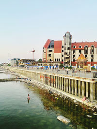 People on river by buildings against clear sky