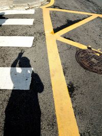 Shadow of person gesturing peace sign on zebra crossing