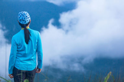 Rear view of woman standing against cloudy sky