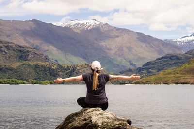 Rear view of man standing on rock by lake against mountains